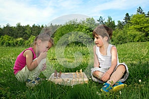 Little Boy And Girl Sitting On The Grass And Playing Chess On Beautiful Spring Day
