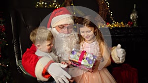 Little boy and girl sitting on the lap of Santa Claus. Christmas present