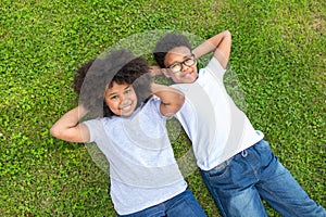 Little boy and girl smiling while lying with hands behind head on the grass in park.