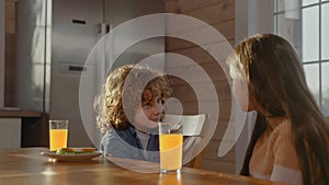 Little boy and girl smiling and talking at breakfast, drinking orange juice