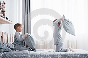 Little boy and girl staged a pillow fight on the bed in the bedroom. Naughty children beat each other pillows. They like