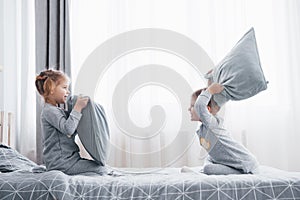 Little boy and girl staged a pillow fight on the bed in the bedroom. Naughty children beat each other pillows. They like