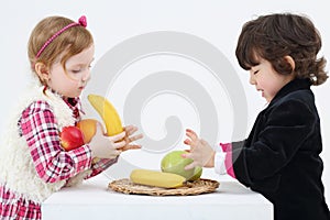 Little boy and girl stand and take fruits from white table