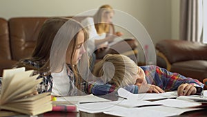 Little boy and girl studying at home in the foreground while their mother sitting in the background. The brother falling