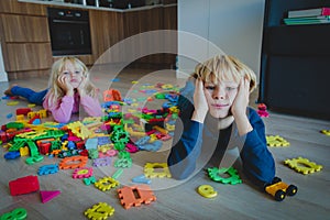 Little boy and girl tired stressed exhausted with toys scattered indoors