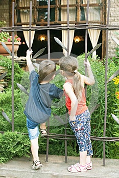 The little boy and girl watches the cafe with curiosity from behind the fence.