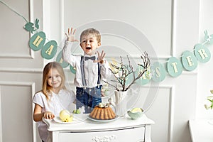 Little boy with a girl in white shirts having fun at the Easter table.