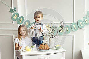 Little boy with a girl in white shirts having fun at the Easter table.