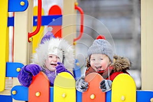 Little boy and girl in winter clothes having fun in outdoors playground