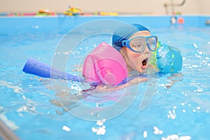 Little boy with glasses and inflatable armbands in swimming pool. Child learning to swim