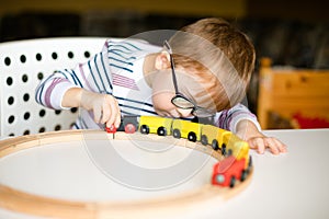 Little boy in the glasses with syndrome dawn playing with wooden railways