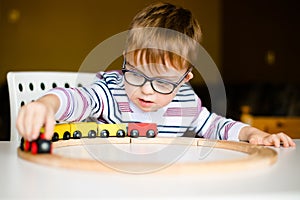 Little boy in the glasses with syndrome dawn playing with wooden railways