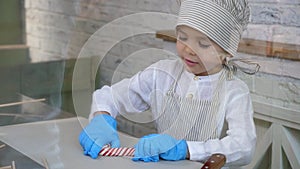 A little boy in gloves and a kitchen uniform makes himself a lollipop on a stick