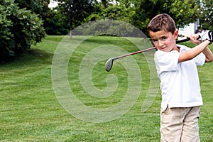 Little boy golfer swinging a club on the golf course