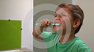 Little boy in green t-shirt cleans his teeth