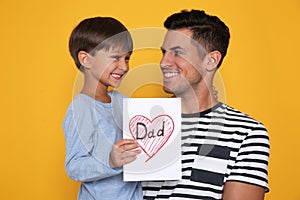 Little boy greeting his dad with Father`s Day on yellow background