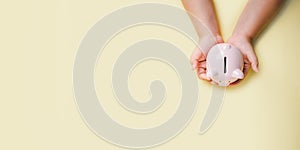 Little boy hand holding piggy bank on yellow background