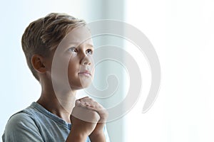 Little boy with hands clasped together for prayer on light background.