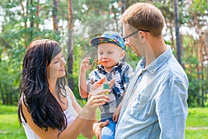 A little boy in the hands of the dad and blow soap bubbles. Mom