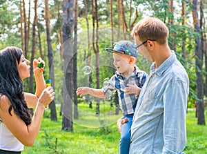 A little boy in the hands of the dad and and his mom blowing soap bubbles.