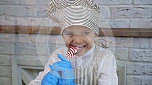 A little boy in a hat and apron bites soft caramel while making handmade candies