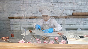 A little boy in a hat and apron makes himself a lollipop made of soft caramel.