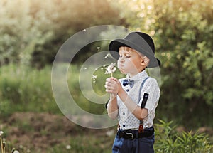 A little boy in a hat blowing on a white dandelion. Child in retro clothing