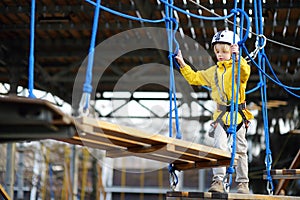 Little boy having fun in Adventure Park for children amoung ropes, stairs, bridges. Outdoor climbing adventure playground in