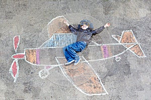 Little boy having fun with airplane picture drawing with chalk