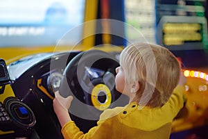 Little boy having fun in amusement in play center. Kid playing racing simulator game in Arcade centre