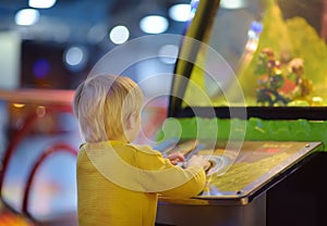 Little boy having fun in amusement in play center. Kid playing on slot machine in Arcade centre