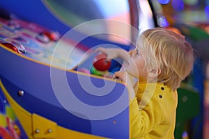 Little boy having fun in amusement in play center. Kid playing on slot machine in Arcade centre