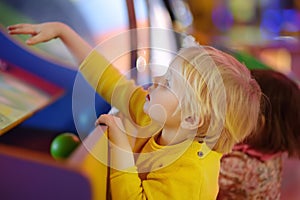 Little boy having fun in amusement in play center. Kid playing on slot machine in Arcade centre