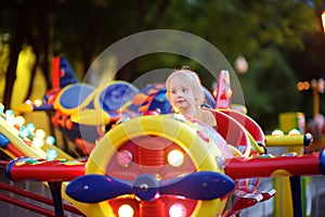 Little boy having fun on attraction in public park. Child riding on a merry go round at summer evening. Attraction, planes, cars,