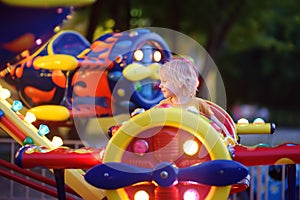 Little boy having fun on attraction in public park. Child riding on a merry go round at summer evening. Attraction, planes, cars,