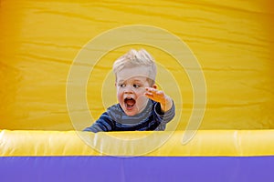 Little boy having fun in inflatable castle playground. Furious child shouts loudly. Bright yellow rubber trampoline background,