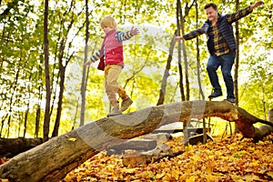 Little boy having fun with mature father during stroll in the forest at sunny autumn day. Active family time on nature