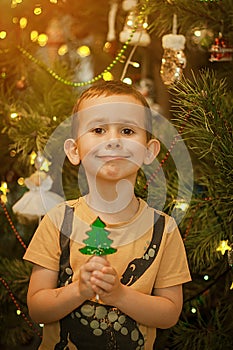 Little boy having fun near a christmas tree with a candy in shape of a fir tree