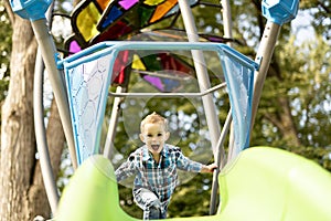 Little boy having fun on a playground outdoors in summer. Toddler on a slide.