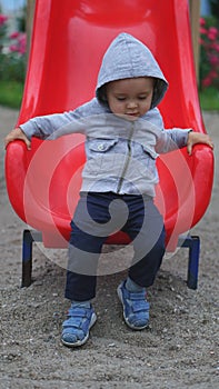 Little boy having fun on a playground outdoors in summer. Toddler on a slide