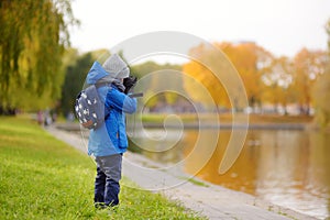 Little boy having fun during stroll in city park at sunny autumn day. Child exploring nature with binoculars