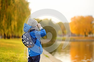 Little boy having fun during stroll in city park at sunny autumn day. Child exploring nature with binoculars. Active outdoor
