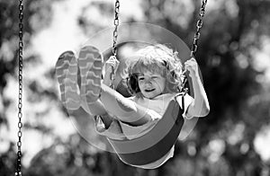 Little boy having fun on a swing on the playground in public park on summer day. Happy child enjoy swinging. Child