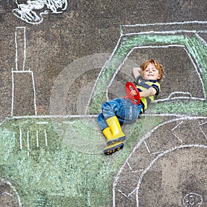 Little boy having fun with tractor picture drawing with chalk