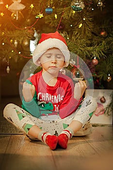 Little boy having fun under a christmas tree dressed in festive pajama and hood