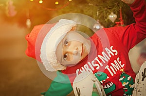 Little boy having fun under a christmas tree dressed in festive pajama and hood