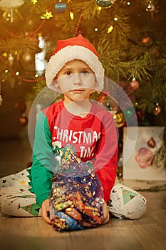 Little boy having fun under a christmas tree dressed in festive pajama and hood