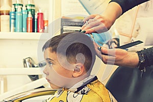 little boy having a haircut at hair salon..Children hairdresser with scissors and comb is cutting little boy. Contented