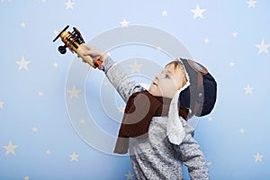 Little boy in helmet and glasses with wooden plane against the background of a blue wall with stars. Happy child playing with toy