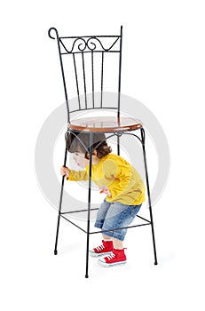 Little boy hides under high wrought-iron chair